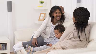 Young mother with child, sitting on couch talking to other woman
