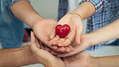 Close up of numerous hands holding a carved red wooden heart