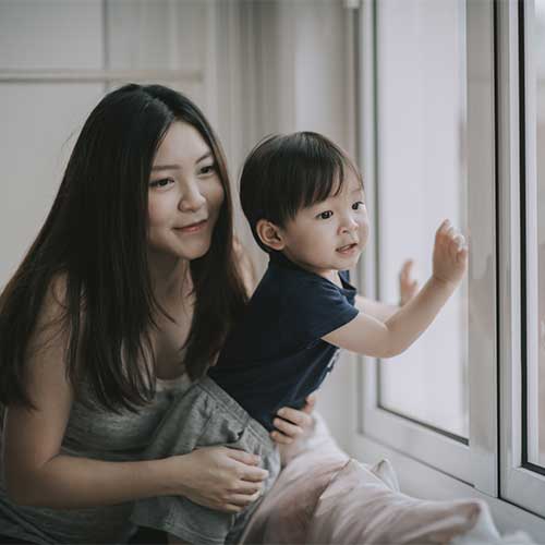Woman holding child, looking out a window